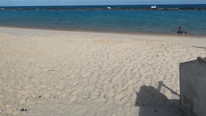 Ein Strand mit klarem, blauem Wasser, einem sandigen Ufer und dem Schatten einer Person.