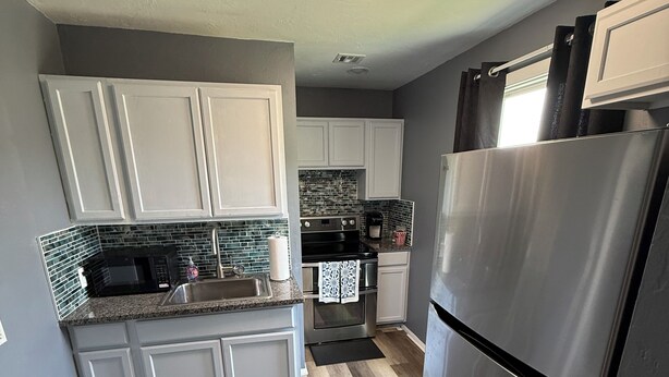 A kitchen with white cabinets, a stainless steel refrigerator, a microwave, and a coffee maker.