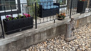 A balcony with a black metal railing, a wicker sofa with blue cushions, and a statue of a child.