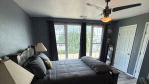 A bedroom with a bed, a ceiling fan, a window, and a door.