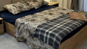 Quarto com cama, mesa de cabeceira, abajur e um enfeite na parede.