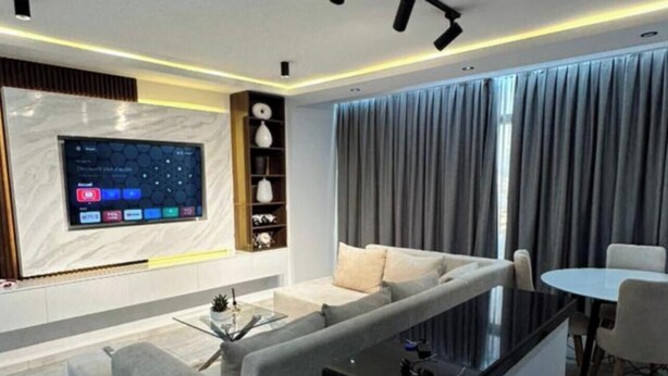 Uma sala de estar moderna com sofá, mesa de centro, TV na parede e área de jantar com mesa e cadeiras.