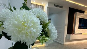 Um interior moderno com uma mesa de vidro, flores brancas num vaso estampado e um design elegante e contemporâneo.