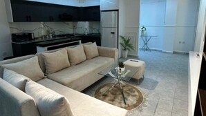 Uma sala de estar moderna com sofá, mesa de centro e área de cozinha ao fundo.