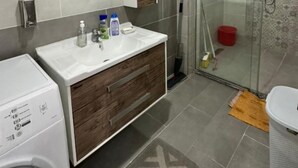 Um banheiro moderno com máquina de lavar embutida, box de vidro e toucador com espelho.