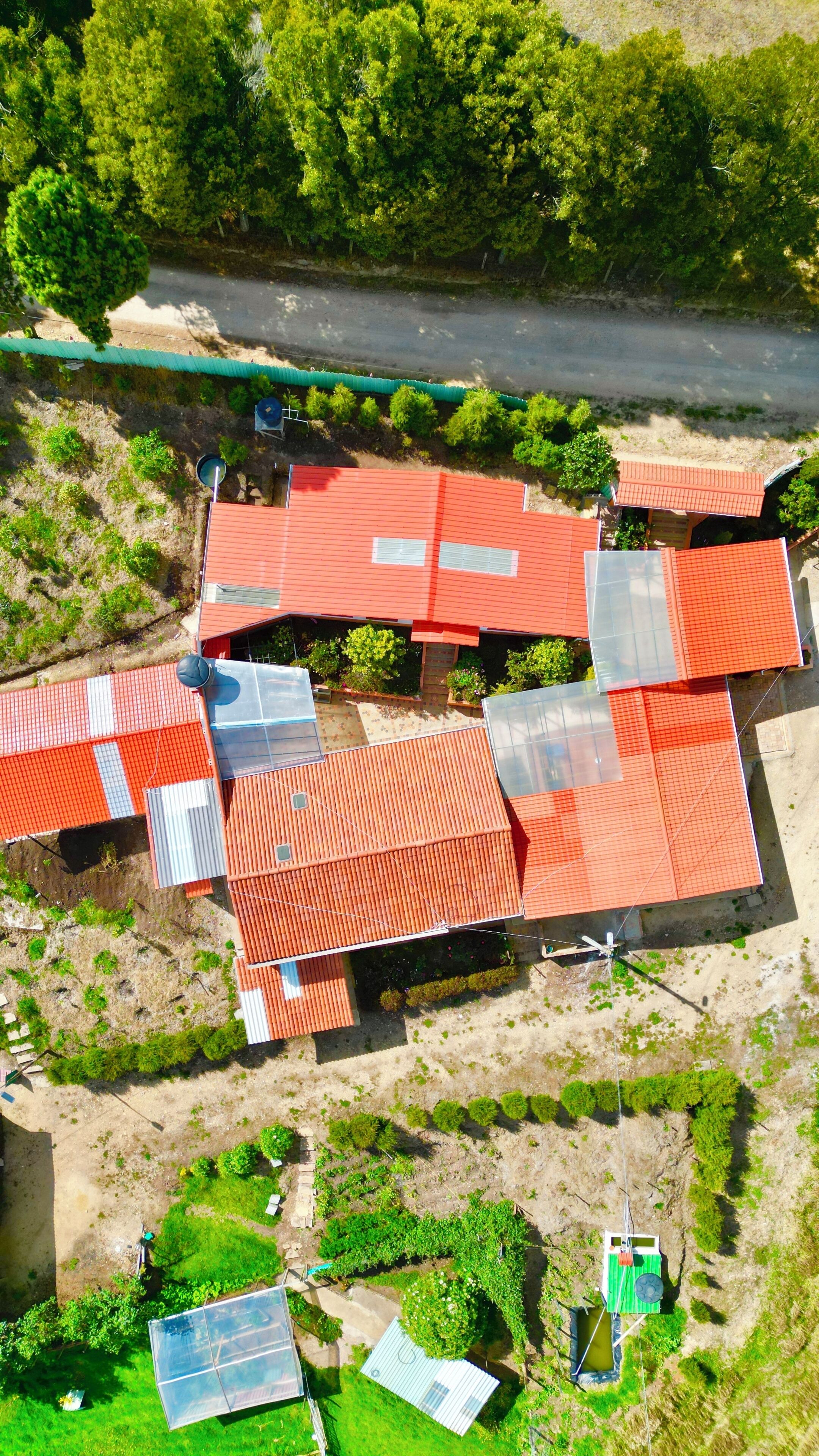 Vista aérea de un edificio con varias secciones de tejados rojos, rodeado de vegetación y una carretera.