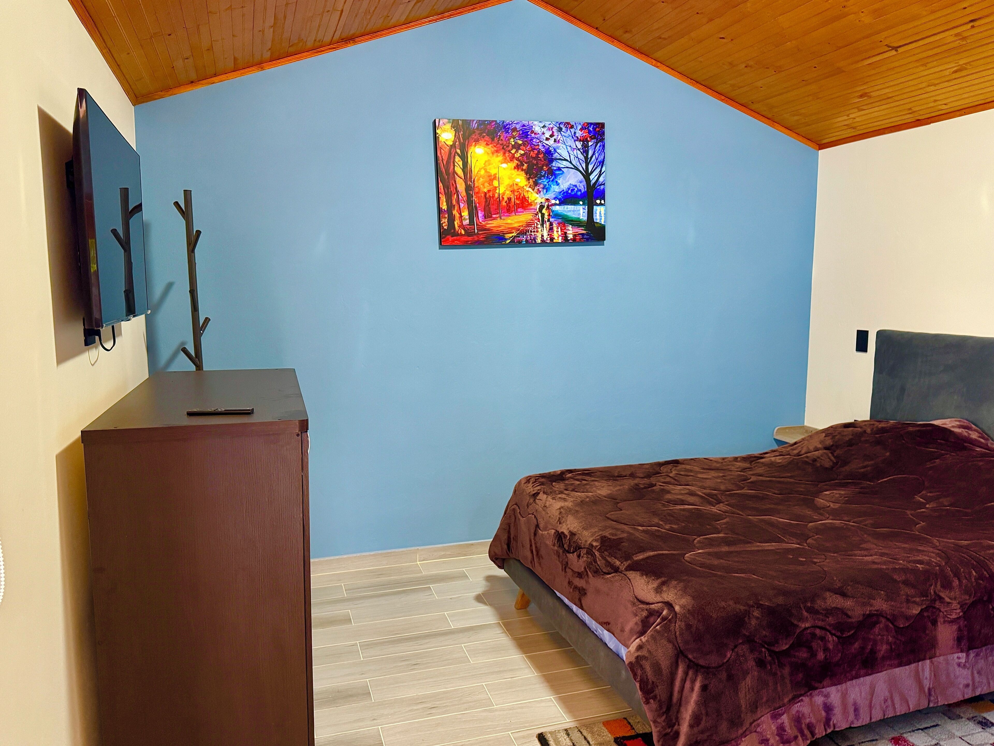 Ein Schlafzimmer mit Bett, Kommode, einem Gemälde an der Wand und Holzboden.