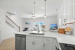 A modern kitchen with white cabinetry, a stainless steel sink, a ceiling fan, pendant lights, and a view of the outside. - Walk to Beach! Brand New Home-Sleeps 10 (Myrtle Beach)
