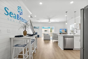 A modern kitchen with white cabinetry, a dining area with stools, a large vase, and a ceiling fan. - Walk to Beach! Brand New Home-Sleeps 10 (Myrtle Beach)