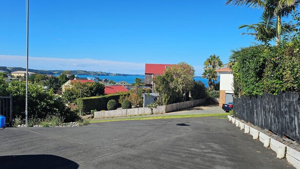 Une rue résidentielle bordée de maisons, un ciel d’un bleu éclatant et une vue sur la mer.