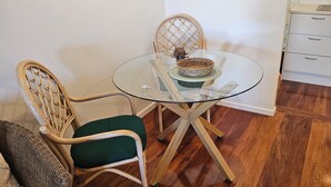 Un coin repas avec une table en verre, des chaises en osier et une cuisine dotée de meubles blancs.