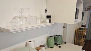 Une cuisine avec une étagère blanche où sont rangés des verres, un grille-pain vert et un panier en bois.