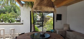Una stanza con un tavolo di legno, un tetto di paglia e vista sulla vegetazione.