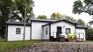 A single-story building with a metal roof, a front porch with a grill, and a small deck area.