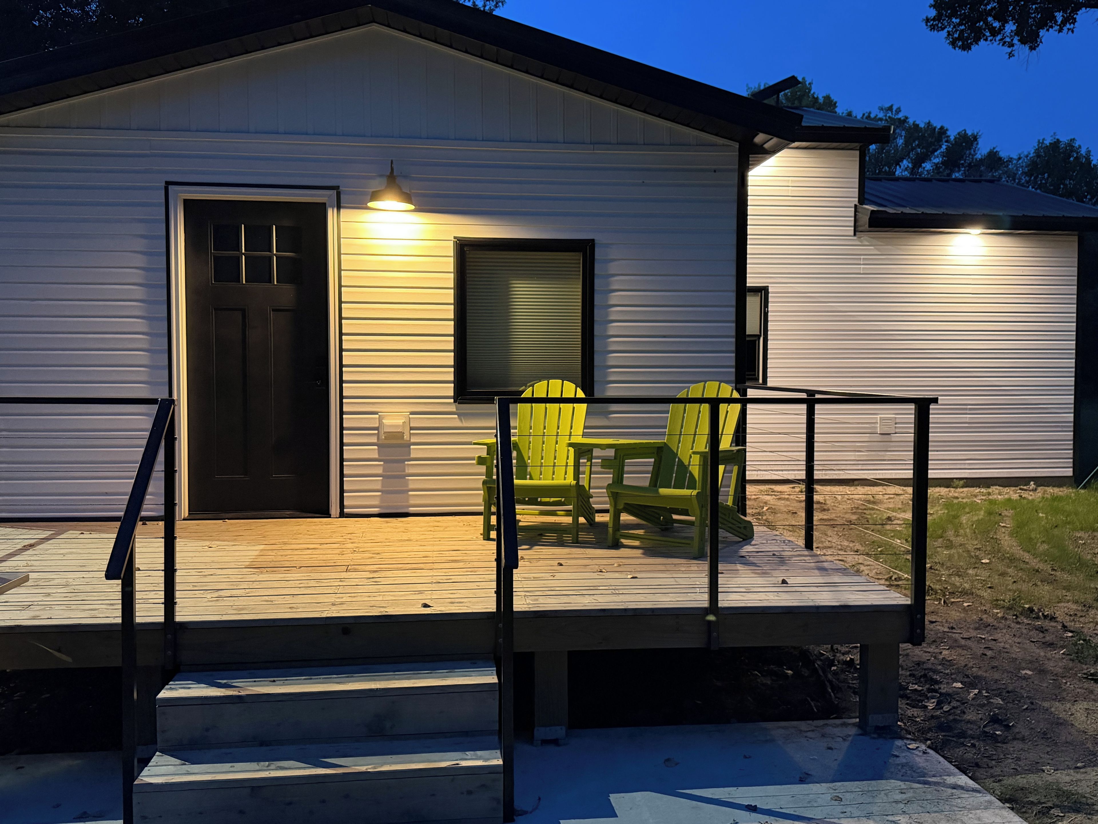 A wooden deck with a railing, a door, and two chairs.