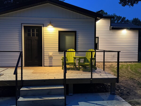 A wooden deck with a railing, a door, and two chairs.