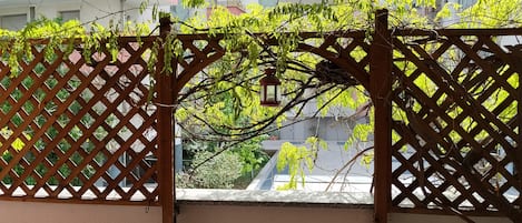 Una reja de madera con un farol colgando, que da acceso a un balcón con vistas a edificios de varios pisos.