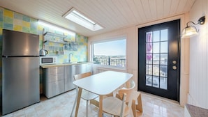 A kitchen with a refrigerator, microwave, and stove, a dining table with chairs, a window with a view, and a door with a window.