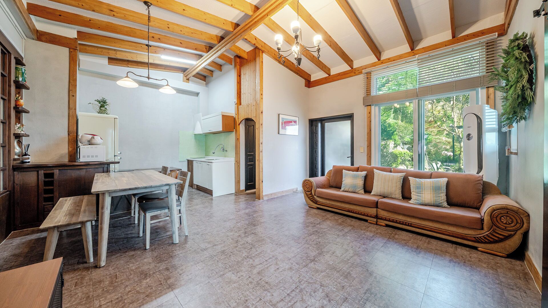 Un amplio salón con techo de madera, una mesa de comedor con sillas, un sofá con cojines y vistas al exterior.