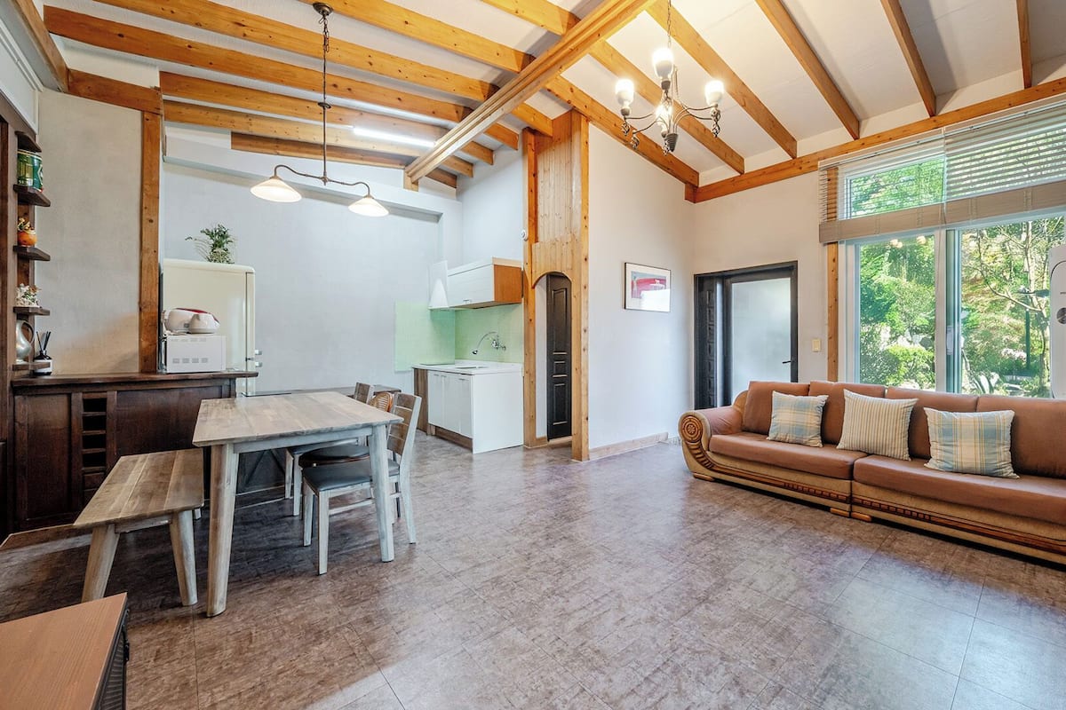 Un amplio salón con techo de madera, una mesa de comedor con sillas, un sofá con cojines y vistas al exterior.