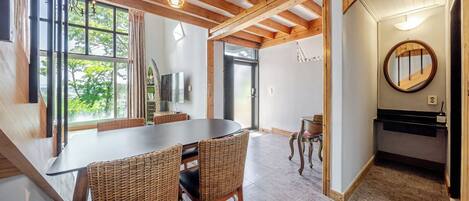 A dining area with a table and chairs, a TV, and a view of greenery outside.