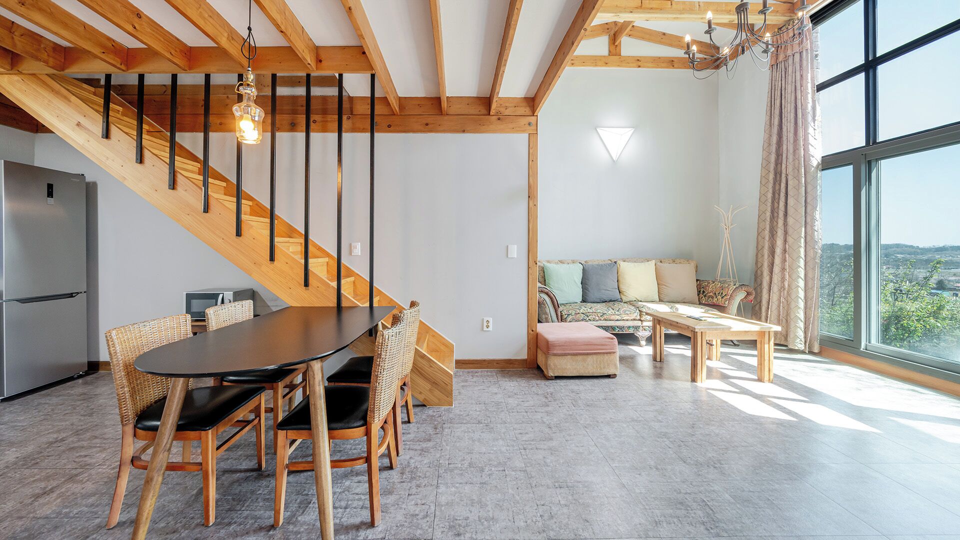 Un interior moderno con zona de comedor, escalera, sofá y ventanas amplias.