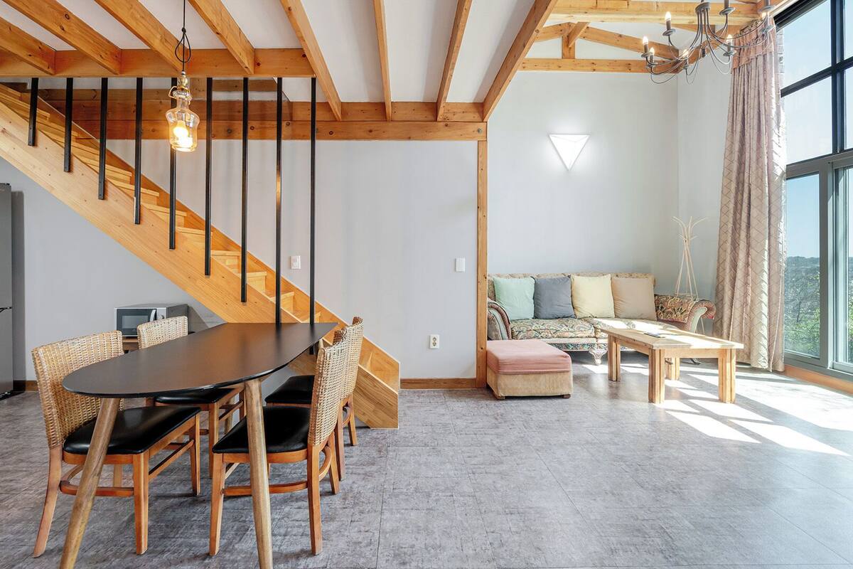 Un interior moderno con zona de comedor, escalera, sofá y ventanas amplias.