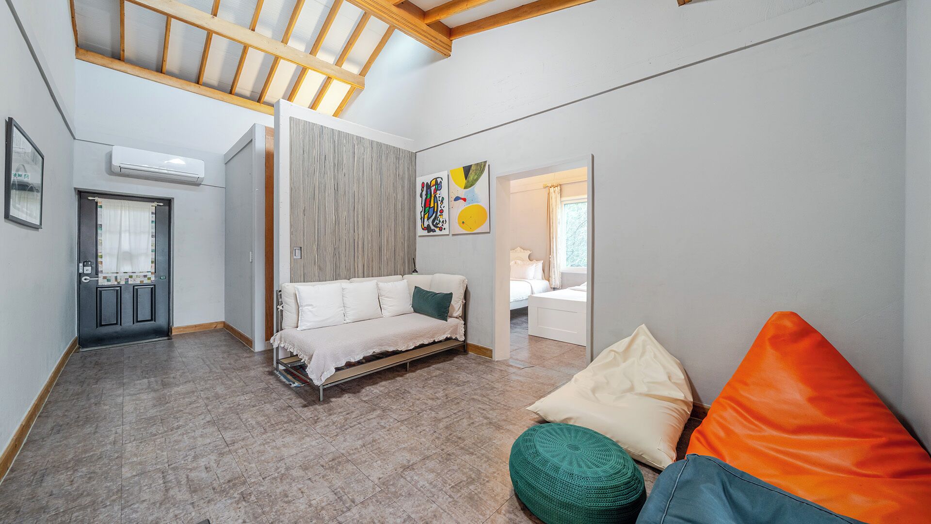 Um interior moderno com sofá, banqueta e cama em um quarto estilo loft com vigas de madeira aparente e teto inclinado.