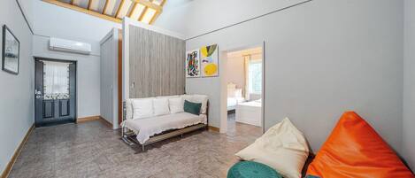 Um interior moderno com sofá, banqueta e cama em um quarto estilo loft com vigas de madeira aparente e teto inclinado.
