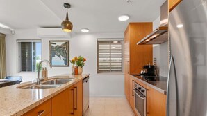 A modern kitchen with a stainless steel refrigerator, wooden cabinets, a granite countertop, a sink, and a pendant light. - Roberts Street Retreat - Taupo CBD (Taupo)