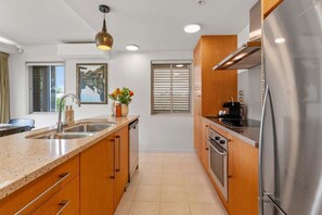 A modern kitchen with a stainless steel refrigerator, wooden cabinets, a granite countertop, a sink, and a pendant light. - Roberts Street Retreat - Taupo CBD (Taupo)