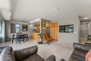 A modern living room with a sofa, a dining area with a table and chairs, a kitchen with wooden cabinets, and a large window. - Roberts Street Retreat - Taupo CBD (Taupo)