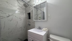 A bathroom with a shower, a sink, a toilet, and a mirror with lights above it.