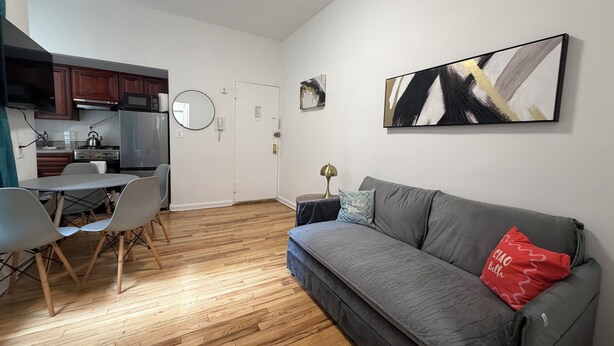 A compact living space with a kitchenette, a dining area, and a sofa with a red pillow.