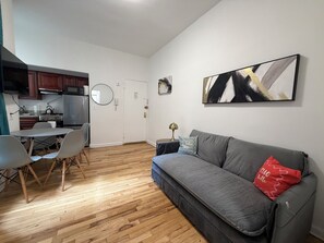 Un espacio habitable compacto con kitchenette, comedor y un sofá con un cojín rojo.