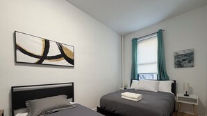 A bedroom with two beds, a window with curtains, and artwork on the walls.
