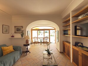 A living room with a sofa, chairs, a glass coffee table, a TV, and a bookshelf. - Domus Floris Positano (Positano)