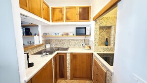 A compact kitchen with wooden cabinets, a microwave, and a tiled backsplash. - Domus Floris Positano (Positano)