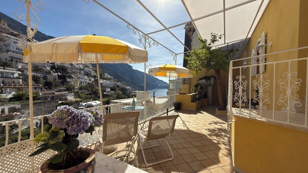 A terrace with outdoor seating, a potted plant, and a view of a coastal town. - Domus Floris Positano (Positano)