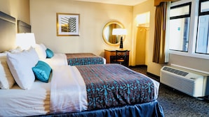 Hotelkamer met twee bedden, een bureau, een stoel, een spiegel, een raam met gordijnen en een wandairconditioner.