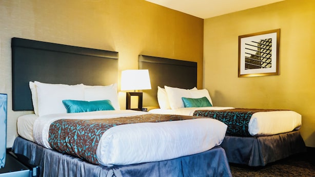 Een hotelkamer met twee bedden, een nachtkastje met een lamp en een lijst aan de muur.