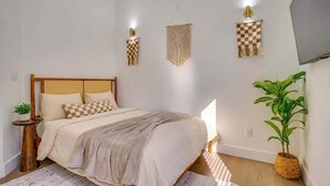 Ein Schlafzimmer mit einem Bett, Nachttischen, Wandleuchten und einer Zimmerpflanze.