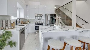 Une cuisine moderne avec des meubles blancs, un îlot en marbre et un escalier en verre.