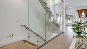 Un intérieur moderne avec un escalier en verre, un plancher en bois et un espace de vie ouvert, agrémenté d’une plante et de meubles.