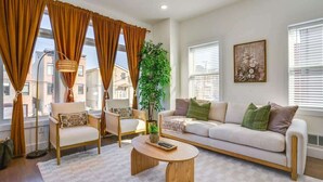 Un salon comprenant un canapé, des fauteuils, une table basse et de grandes fenêtres avec des rideaux.
