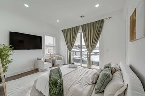 A modern hotel room with a large bed, a flat-screen TV, a sofa, and a balcony with a city view. - Luxury Mansion, Rooftop, Parking, Near NYC & EWR (Jersey City)