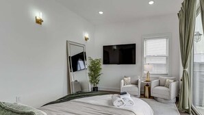 Ein Hotelzimmer mit Bett, Fernseher, Pflanze, Sitzecke und einem fenster mit Vorhängen.