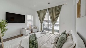 Ein modernes Hotelzimmer mit einem großen Bett, einem Flachbildfernseher, einer Couch und einem Balkon mit Blick auf die Stadt.