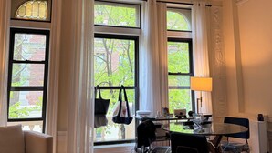 Ein Zimmer mit einer Chandelier, großen Fenstern mit Vorhängen, einem Esstisch mit Stühlen und Blick auf Grünflächen.