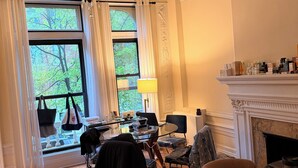 Ein Raum mit einer Chandelier, einem Kamin, einem Esstisch mit Stühlen und Blick auf Bäume durch große Fenster.